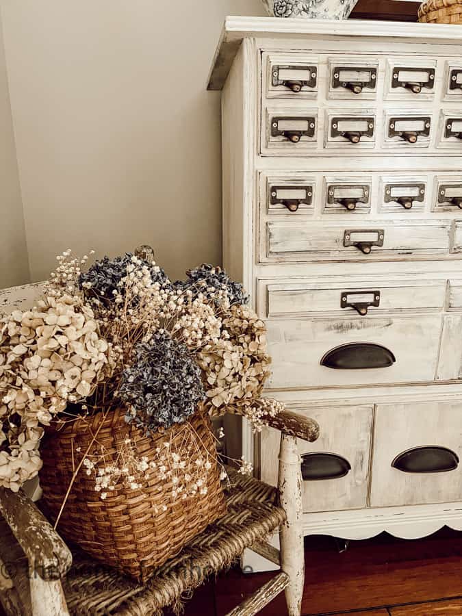 Vintage child's chair holds a vintage basket filled with dried hydrangeas for bedroom decor ides.