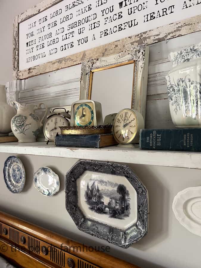 Old clocks above bed with a mirror behind them and antique platters and pitchers for farmhouse decorating.