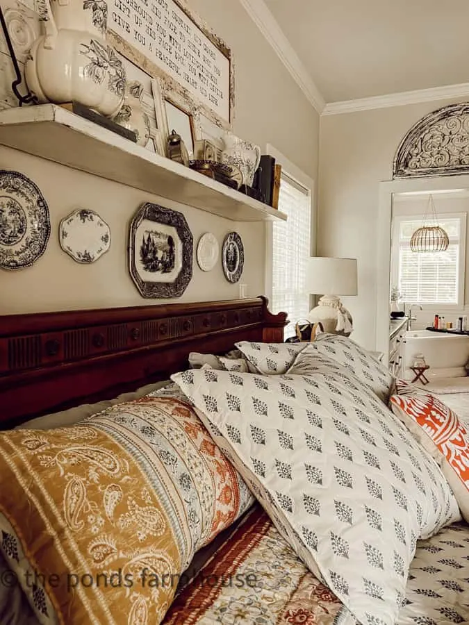 Plates and platters make a gallery wall above the bed in bedroom.  