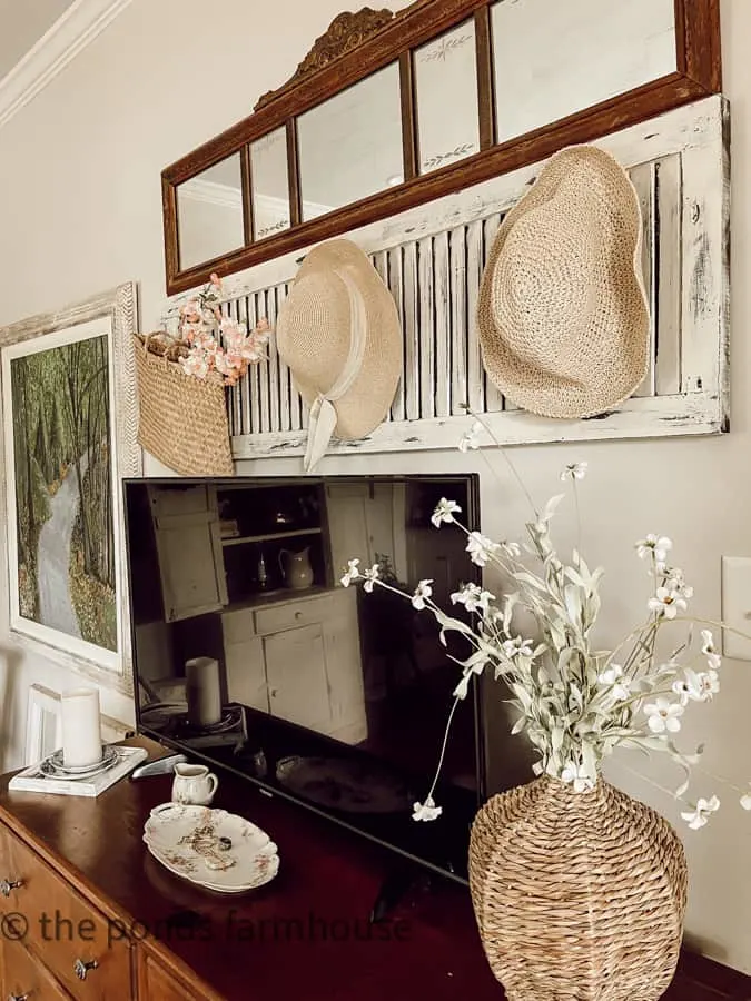 woven vase with faux flowers and straw hats on an old shutter above the tv.  
