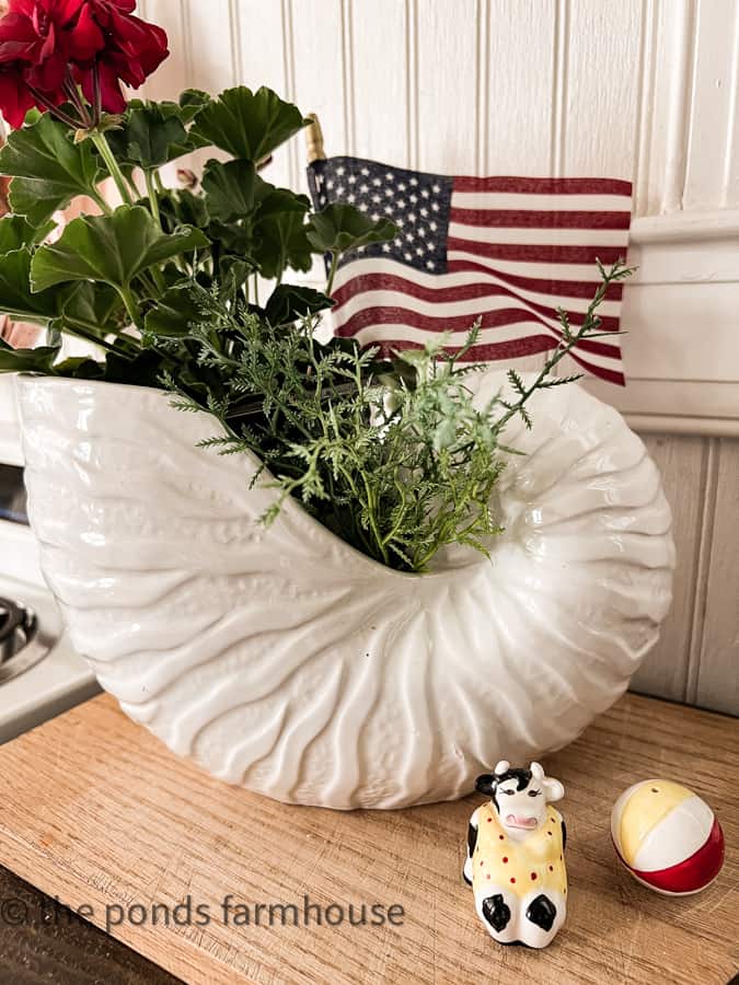 Shell planter with geraniums and flag for patriotic decorating and vintage cow and beach ball salt and pepper shakers. 