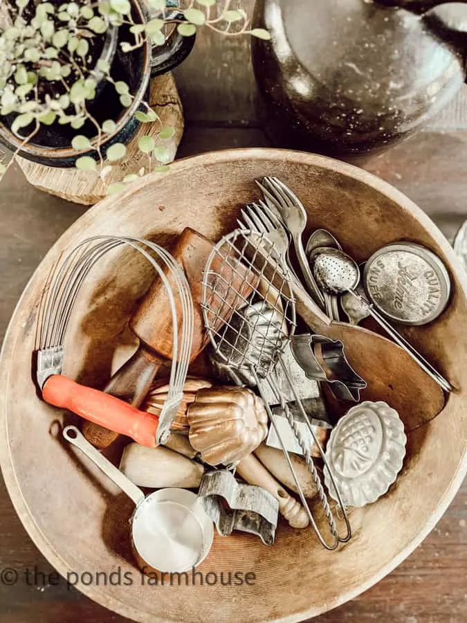 Small vintage kitchen utensils are in a large old wooden bowl.