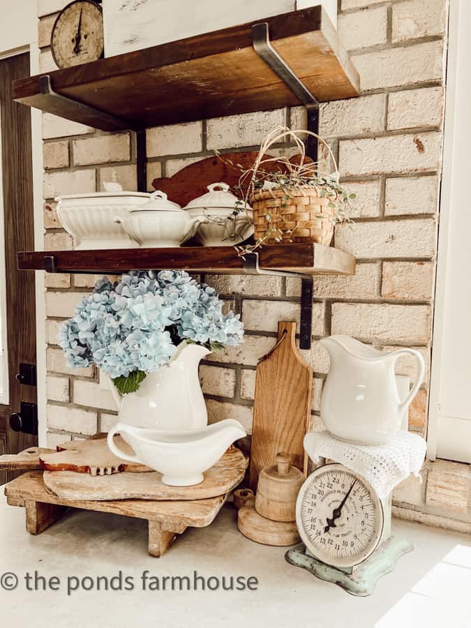 Open shelving filled with budget thrift store decor and vintage collectibles of ironstone and breadboards
