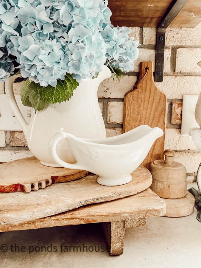 Ironstone pitcher filled with fresh hydrangeas on stacks of breadboards.