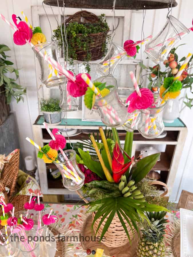 Light fixture decorated for Hawaiian themed Party with flamingo and pineapple straws in glass vases.  Over table.  