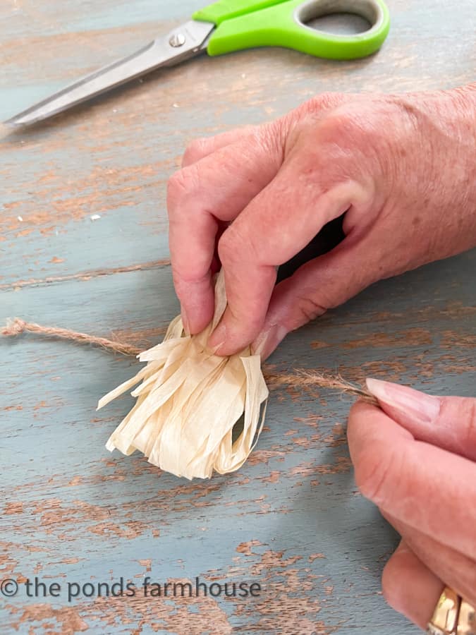 Tie jute twine around raffia to make cheap pom poms for tropical napkin rings dupe.