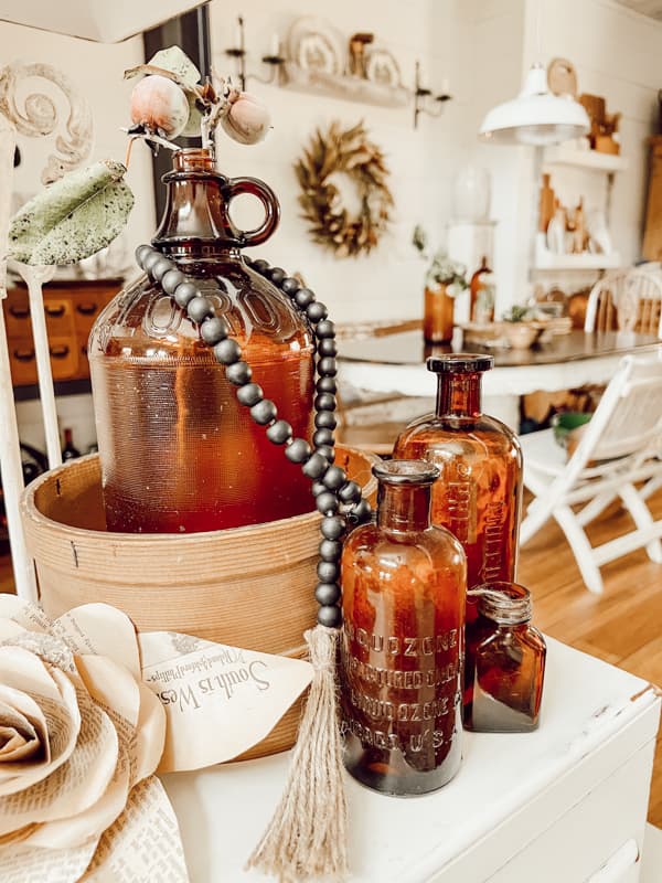 Antique  Bottles on side table with bead garland, DIY paper flowers and vintage sifter.