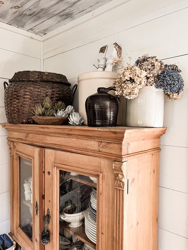 Dried flowers in vintage crock and thrift store basket on top of pine hutch for country chic farmhouse decor.