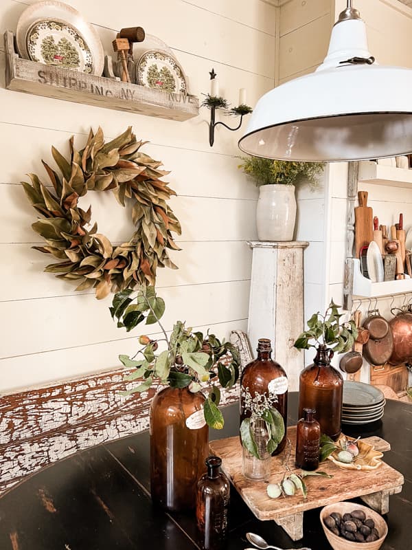 DIY magnolia wreath with wildflowers in a vintage crock and Amber bottles filled with foraged persimmons on old cheese board.