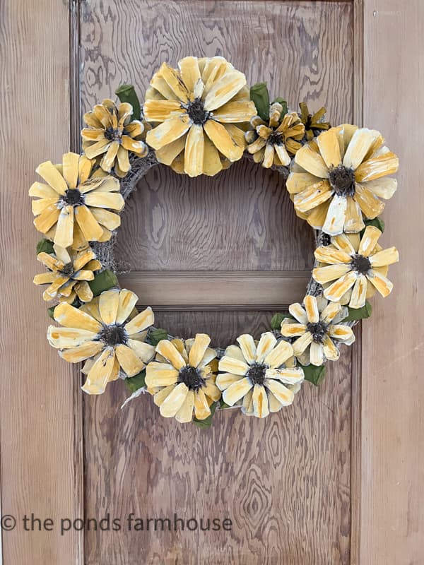 DIY Sunflower Wreath made from pinecones hanging on farmhouse door.