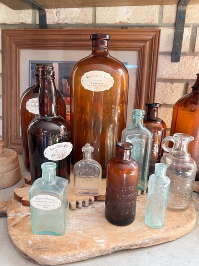 Old amber bottles and blue glass bottles on old bread board in farmhouse kitchen.