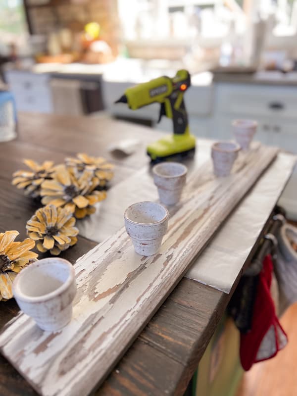 Attach white washed clay pots to the reclaimed wooden board to make pinecone flower art for centerpiece