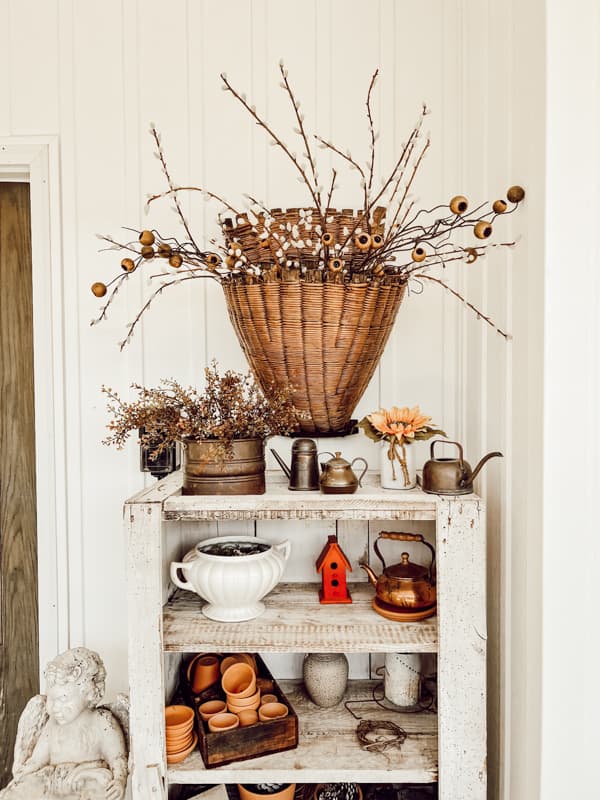 thrifted gathering basket filled with simple stems over a primitive cabinet on farmhouse porch.  