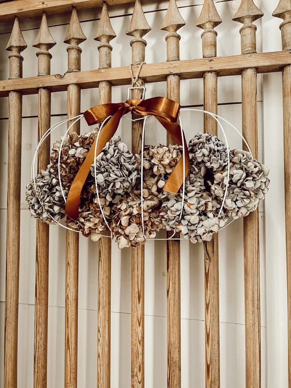 Dollar Tree craft pumpkin with dried Hydrangeas hanging on vintage door for elegant rustic farmhouse style eco-friendly decor.