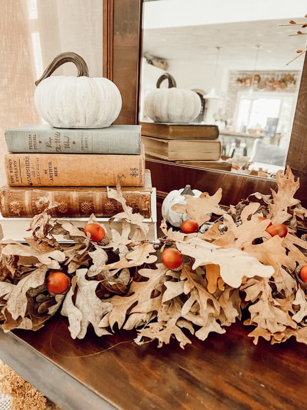 Twig and dried flower arrangement  with vintage books and a pumpkin and an antique mirror. 