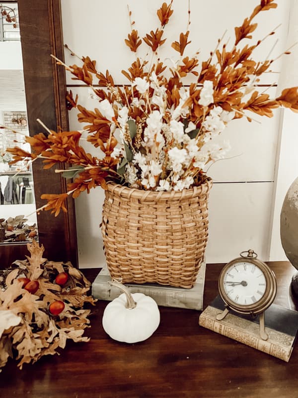 Handcrafted basket filled with faux fall stems on a book for a riser.  