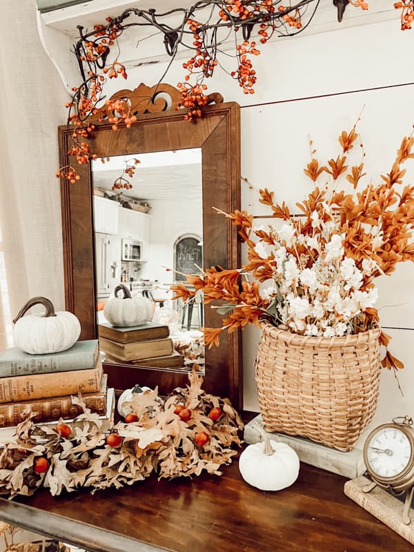 Vintage vignette with antique mirror and handcrafted basket filled with faux stems for fall.