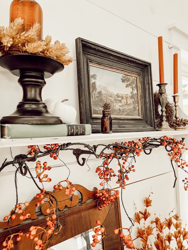 The shelf above entry table with thrifted art and vintage brass candlesticks, bitter sweet garland for fall vignette.