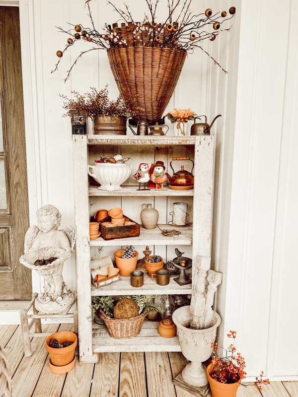 Primitive cabinet with large basket filled with dried stems on farmhouse front porch