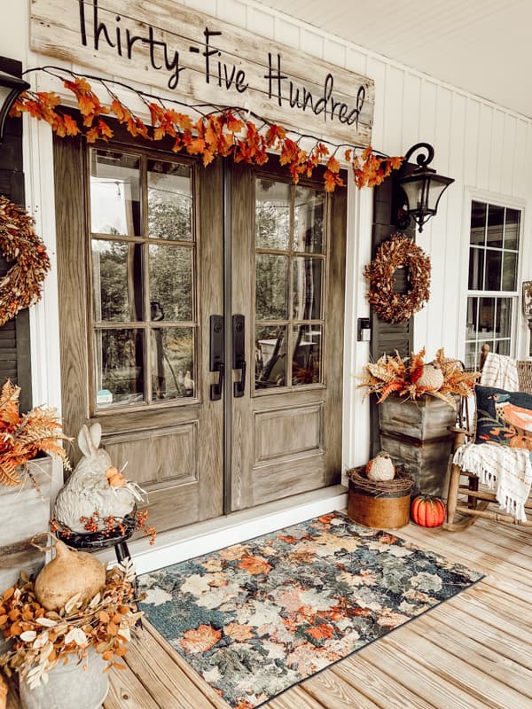 French doors surrounded by leaf garland, bunny tails boxwood wreaths and autumn leaves rug with planters.