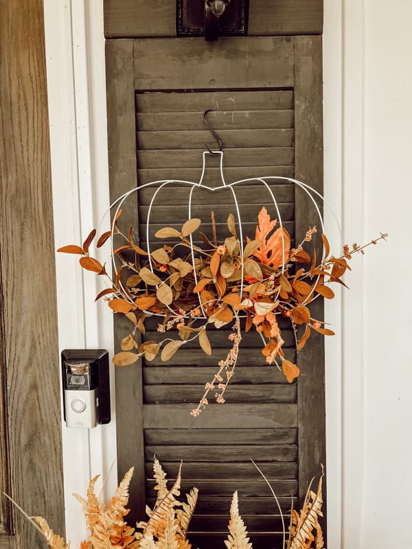 Dollar Tree wire pumpkin crafted with faux twigs and fall leaves on a shutter for budget-friendly fall decorating.