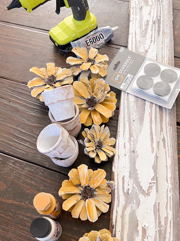 supplies to make a DIY sunflower centerpiece using pinecones and reclaimed shiplap wood.  