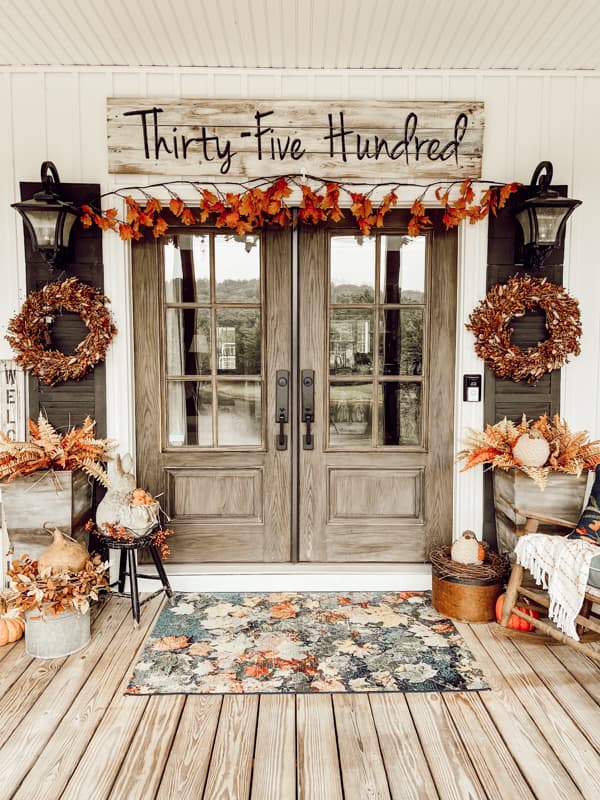 French doors surrounded by leaf garland, bunny tails boxwood wreaths and autumn leaves rug with planters.