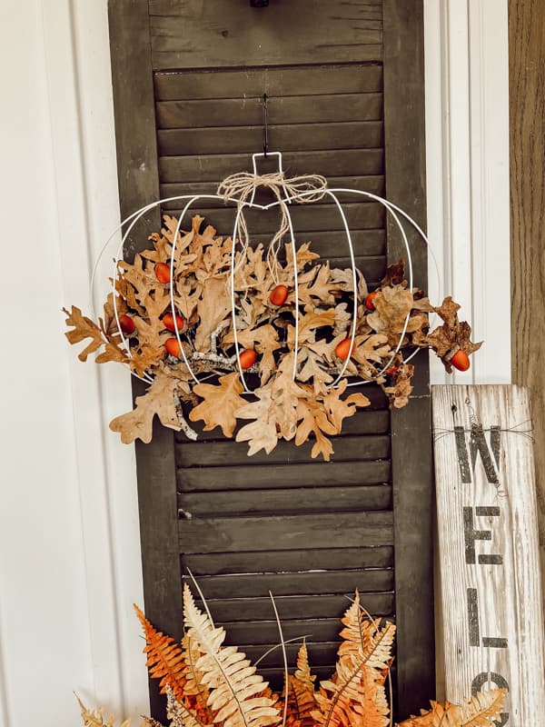 Dollar Tree DIY wire pumpkin wreath with foraged leaves hanging on black shutters. Elegant rustic eco-friendly, sustainable DIY project