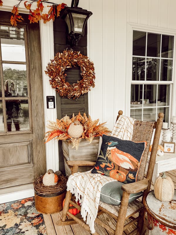 French doors surrounded by hand hooked pillows, bunny tails boxwood wreaths and autumn leaves rug with planters.
