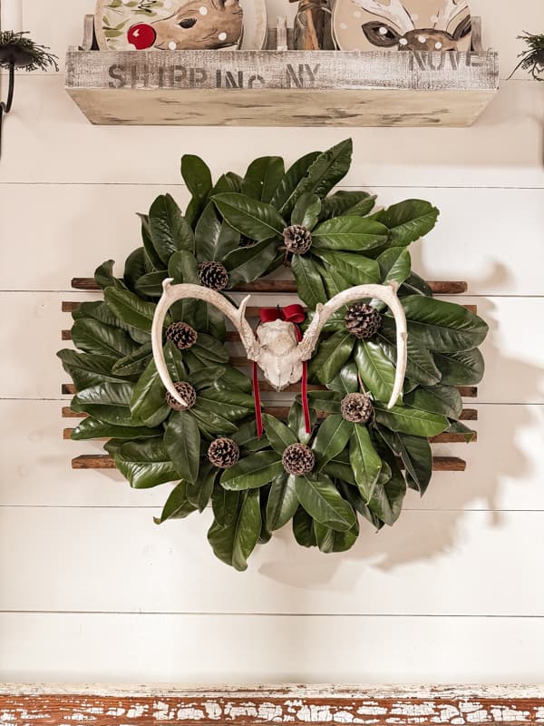 Christmas Wreath hanging on a shiplap wall for a rustic cabin holiday feel, made with natural elements of foraged pinecones & Magnolia