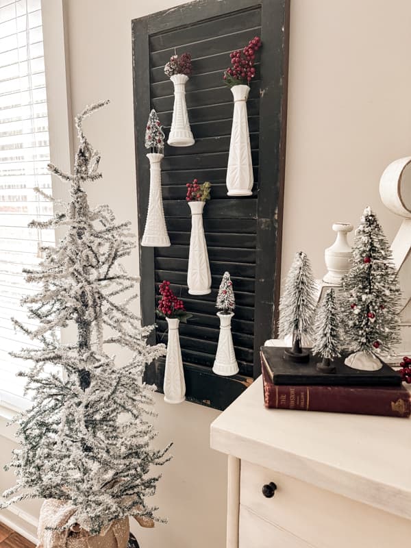 vintage milk glass bud vases hanging on an old shutter decorated for Christmas.  