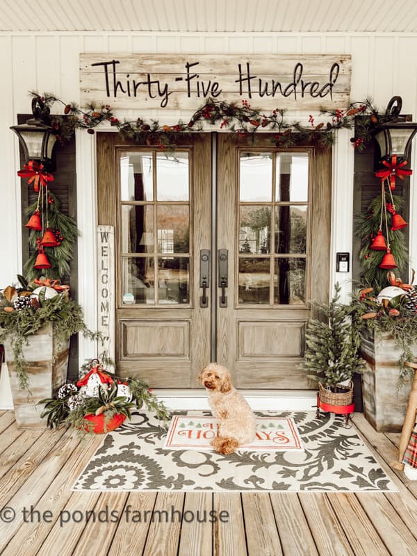 Rustic Farmhouse Front Porch decorated with red bells and DIY address sign. Mini golden Doodle.