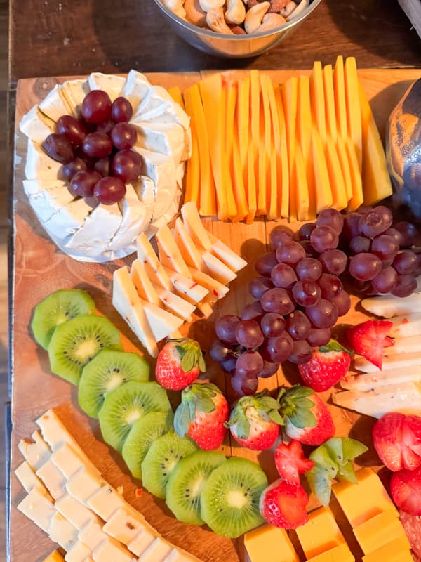 cheese, grapes, strawberries, kiwii, brie on a large wooden board for a grazing table.  