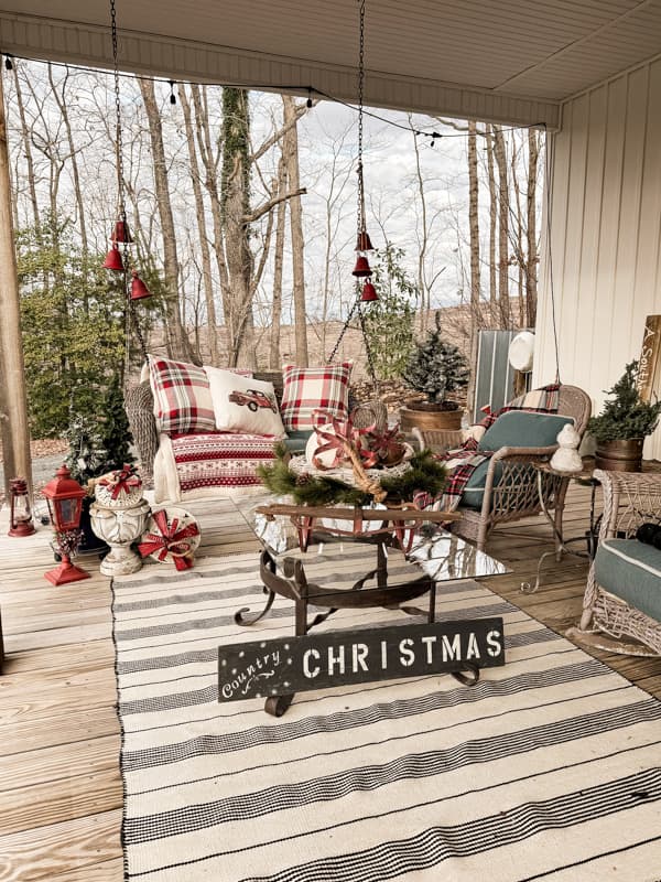 Farmhouse Front Porch Swing with bells and wicker furniture decorated for Christmas. 