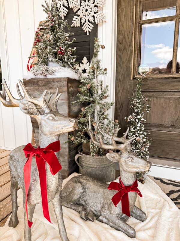 two large reindeer with red bows on a white fur throw blanket on Farmhouse porch.