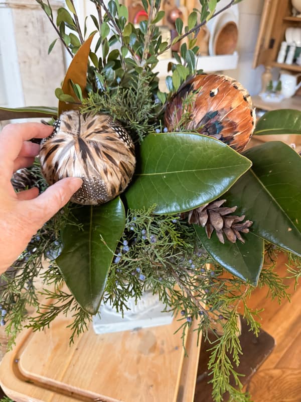 Add feather ornaments with hot glue and tuck in pinecone for a Rustic-Chic Greenery Centerpiece With Feathers Idea. 