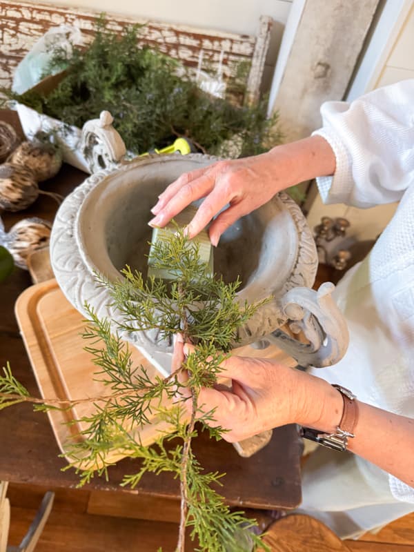 Add the cedar stems to the side of the styrofoam in the large urn.