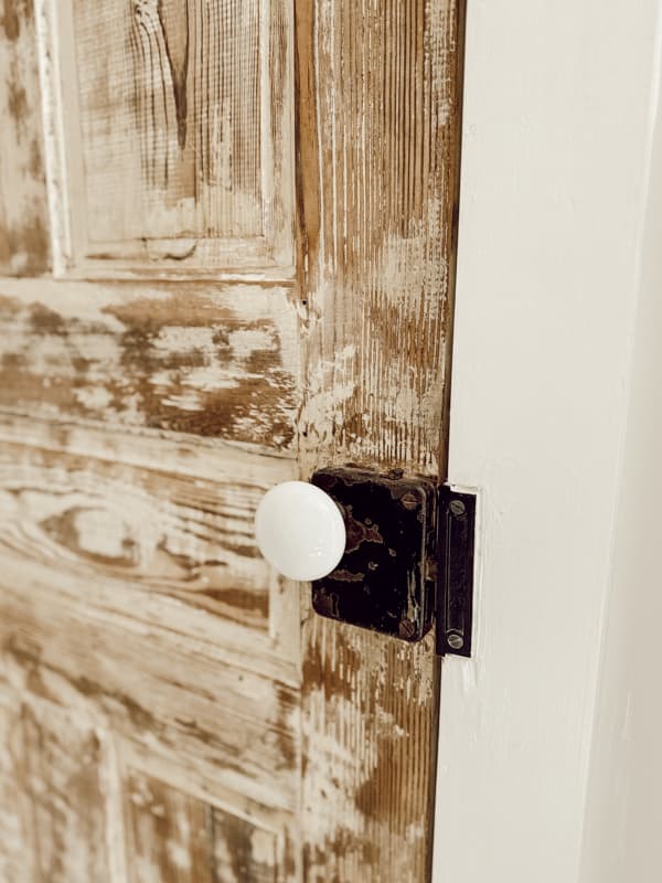 Antique porcelain door knobs on antique door in bathroom of modern farmhouse.  