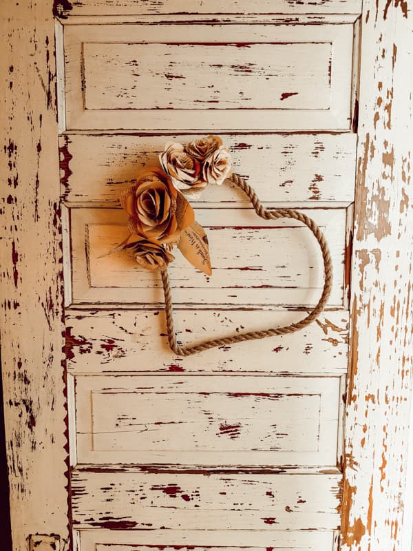 Jute wrapped Dollar Tree Heart Frame with DIY paper Roses on chippy old door.  Easy cottagecore craft.