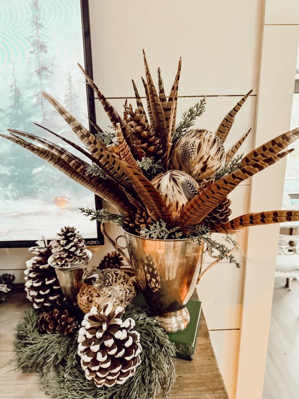 winter mantel Decor with frosted pinecones, pheasant fealther and pinecone arrangement in a silver urn. 