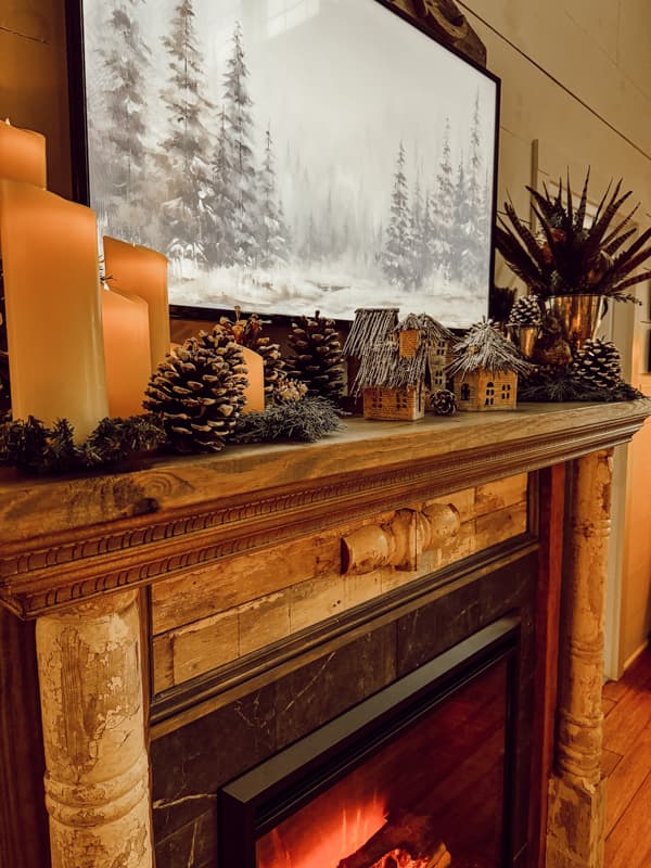 Faux shabby chic fireplace mantel decorated for winter with flicker candles, pinecones, and a old world village.