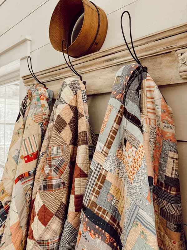 Vintage quilts handing on a pegboard rack. with an old sifter and shiplap walls. 