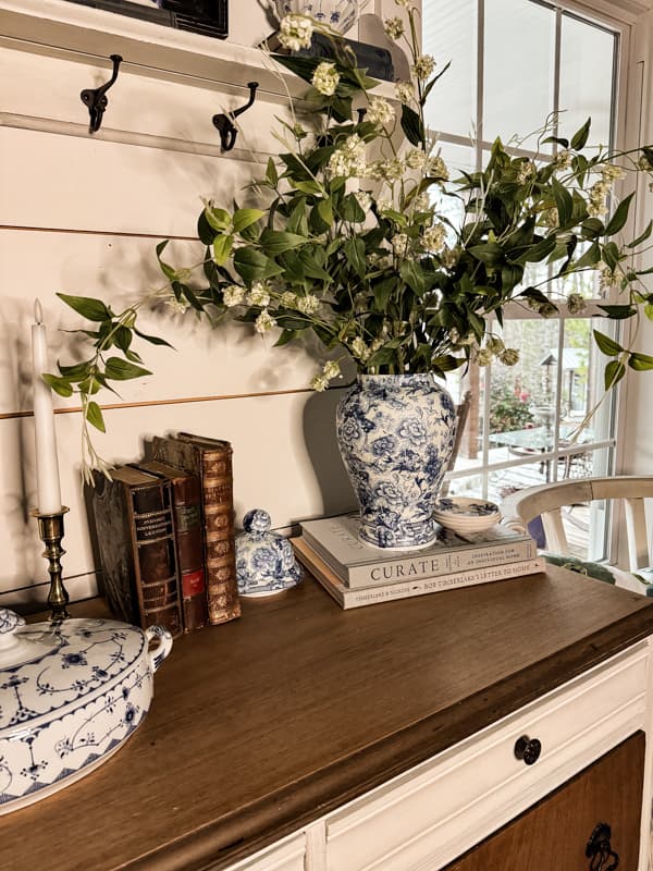 Vase with greenery and flowers on entry table with other blue and white accessories.  