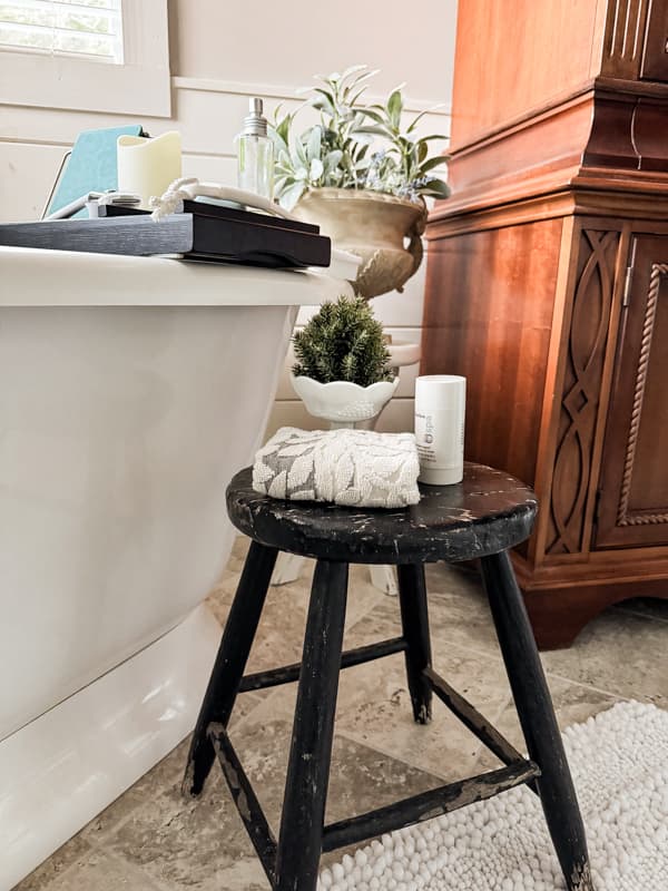 Black chippy stool hold bathroom toiletries in a vintage modern farmhouse 