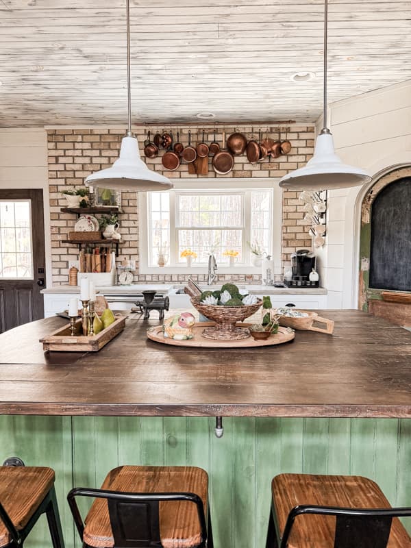 Kitchen island and vintage lights against a brick wall with vintage copper pots. 