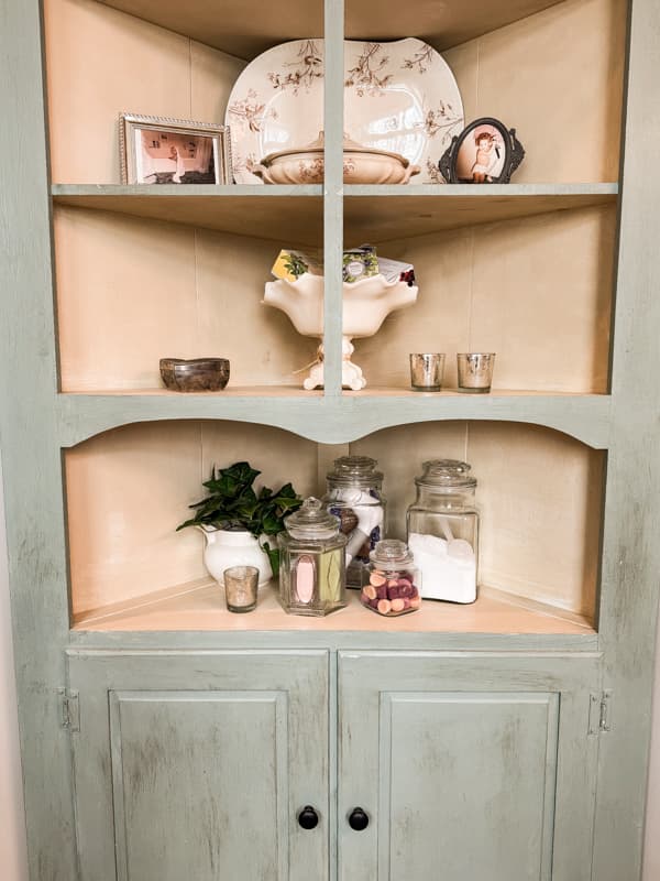 Vintage corner cabinet in modern bathroom filled with bathroom accessories and apothecary jars.  