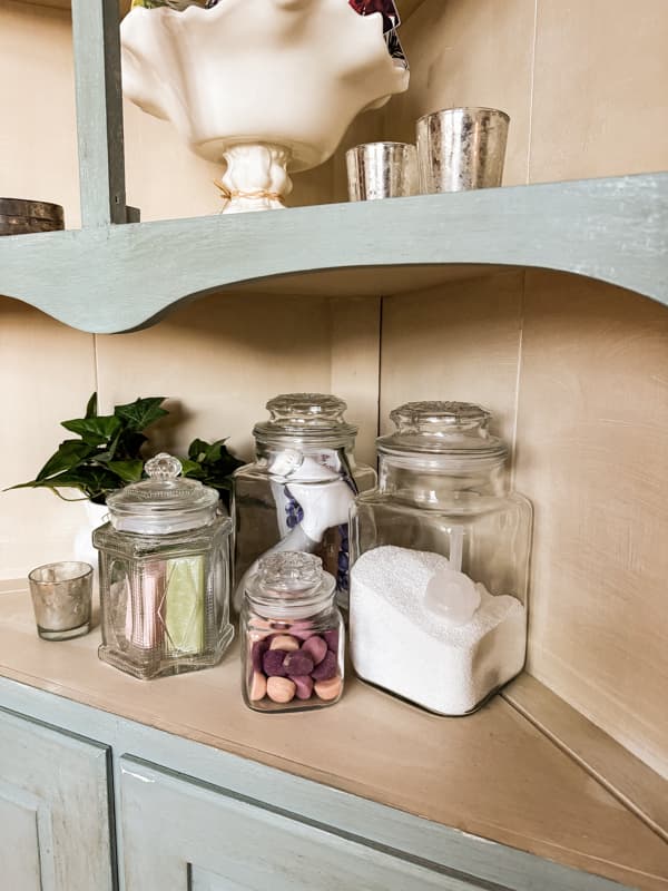 Thrifted Apothecary Jars filled with bath soaps on a antique corner cabinet in vintage modern bathroom.