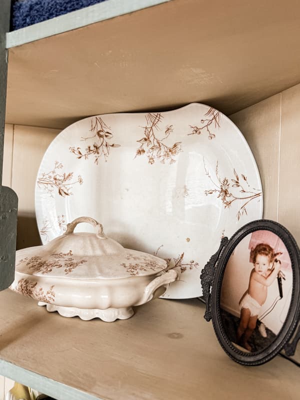 Vintage transferware platter and tureen in corner cabinet of modern bathroom.