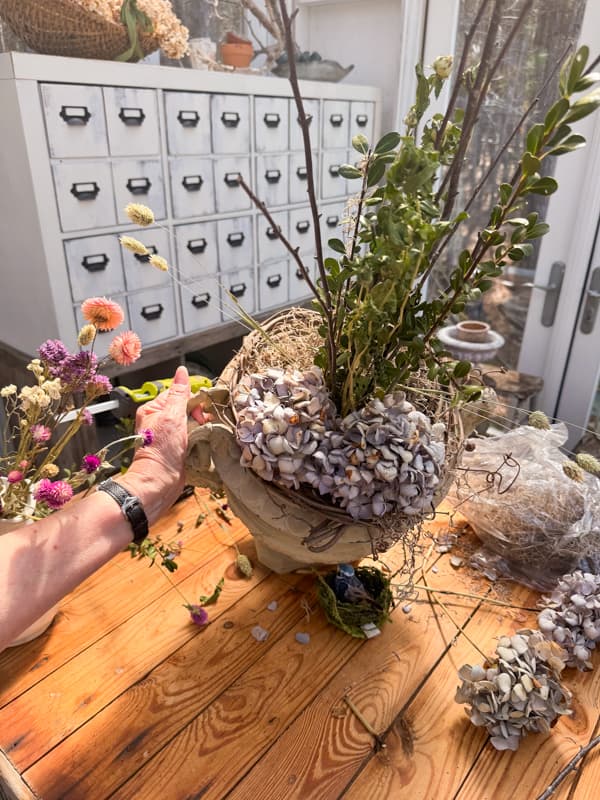 Add twigs and box surrounded by hydrangeas in a large urn in DIY greenhouse.