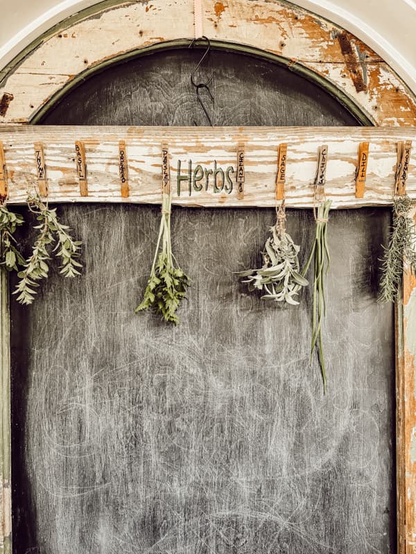 Chippy old board upcycled into a rustic herb drying rack hanging on chippy pantry door.